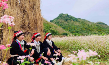 Traditional H'mong women in colorful attire sitting in a flower field.