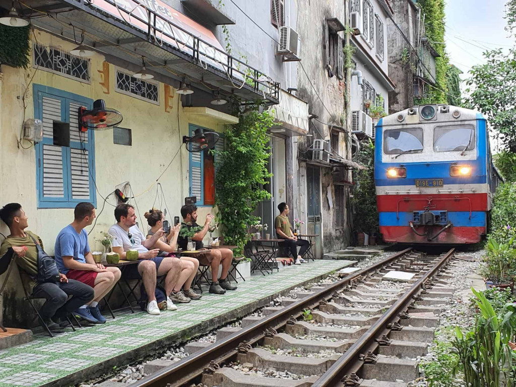 Hanoi street cafe scene with travelers enjoying local drinks near train tracks.