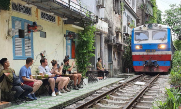 Hanoi street cafe scene with travelers enjoying local drinks near train tracks.