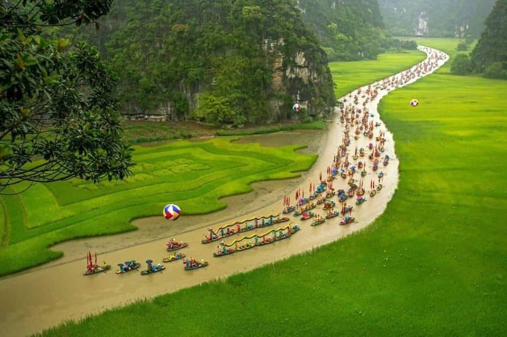 Halong Bay river cruise with colorful boats and lush green scenery.