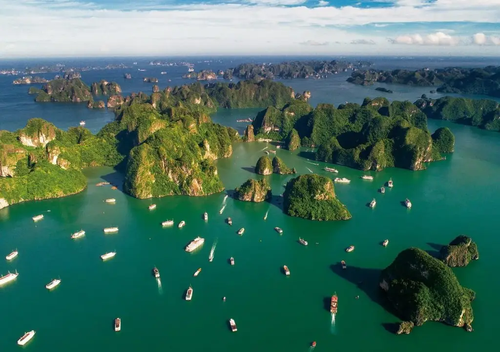 Halong Bay boat tour with numerous islands and boats in emerald waters.