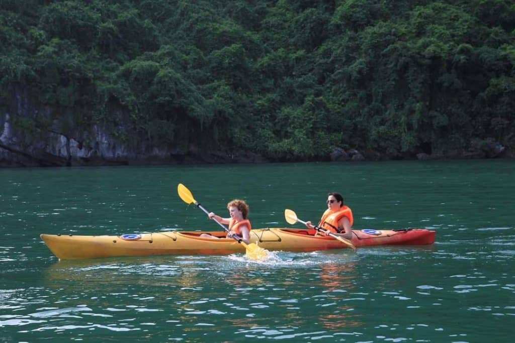 Kayaking activity on Halong Bay with two people paddling in a yellow kayak amidst scenic limestone k.