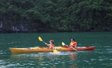 Kayaking activity on Halong Bay with two people paddling in a yellow kayak amidst scenic limestone k.