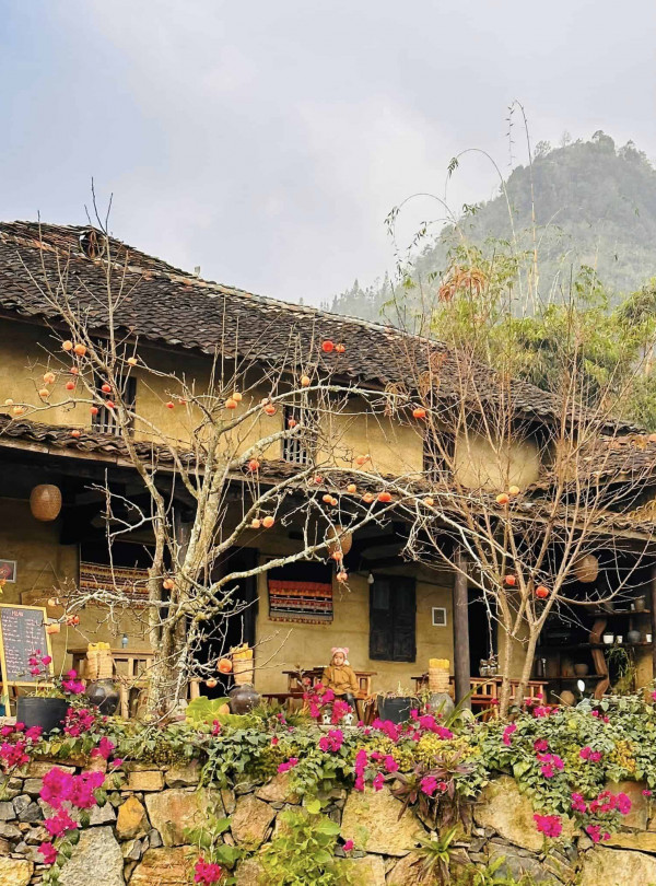 Traditional village house with blooming flowers and mountain backdrop.