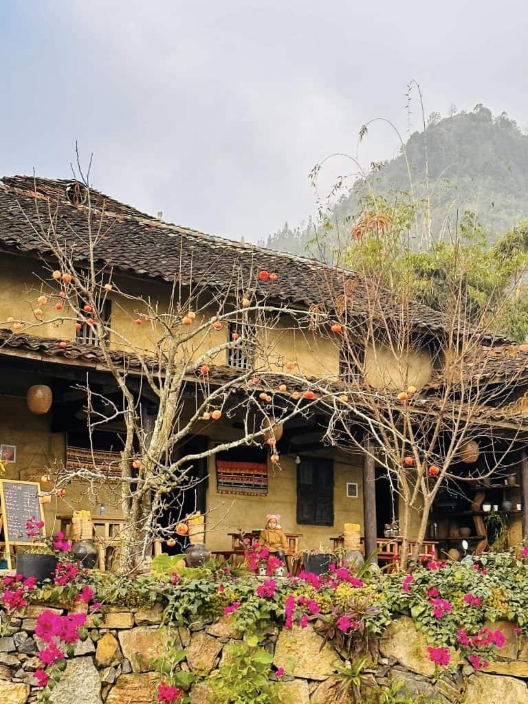Traditional village house with blooming flowers and mountain backdrop.