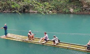 Bamboo raft floating on serene river surrounded by lush greenery, perfect for a peaceful escape.