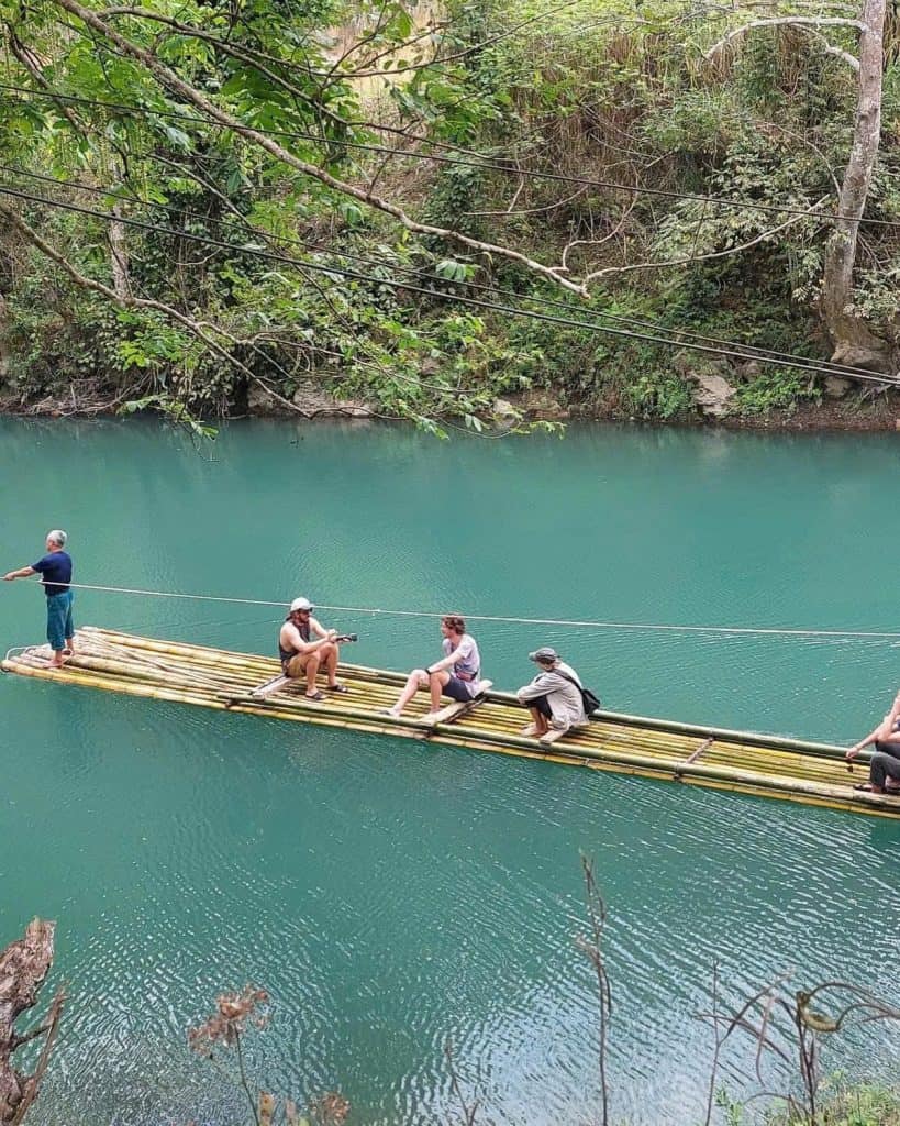 Bamboo raft floating on serene river surrounded by lush greenery, perfect for a peaceful escape.