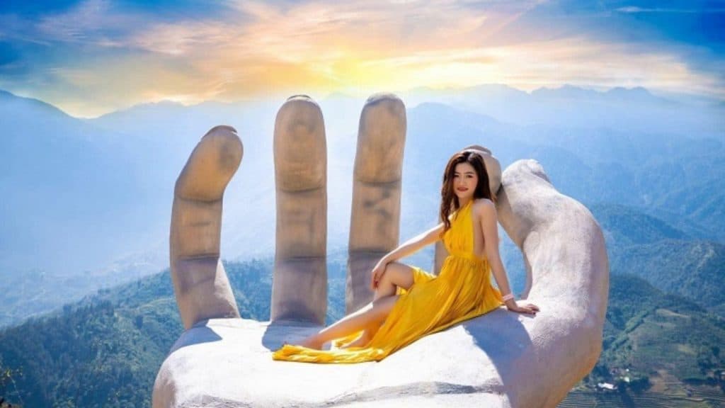 Sunset viewpoint with mountain landscape and a woman in yellow dress sitting on a giant hand sculptu.