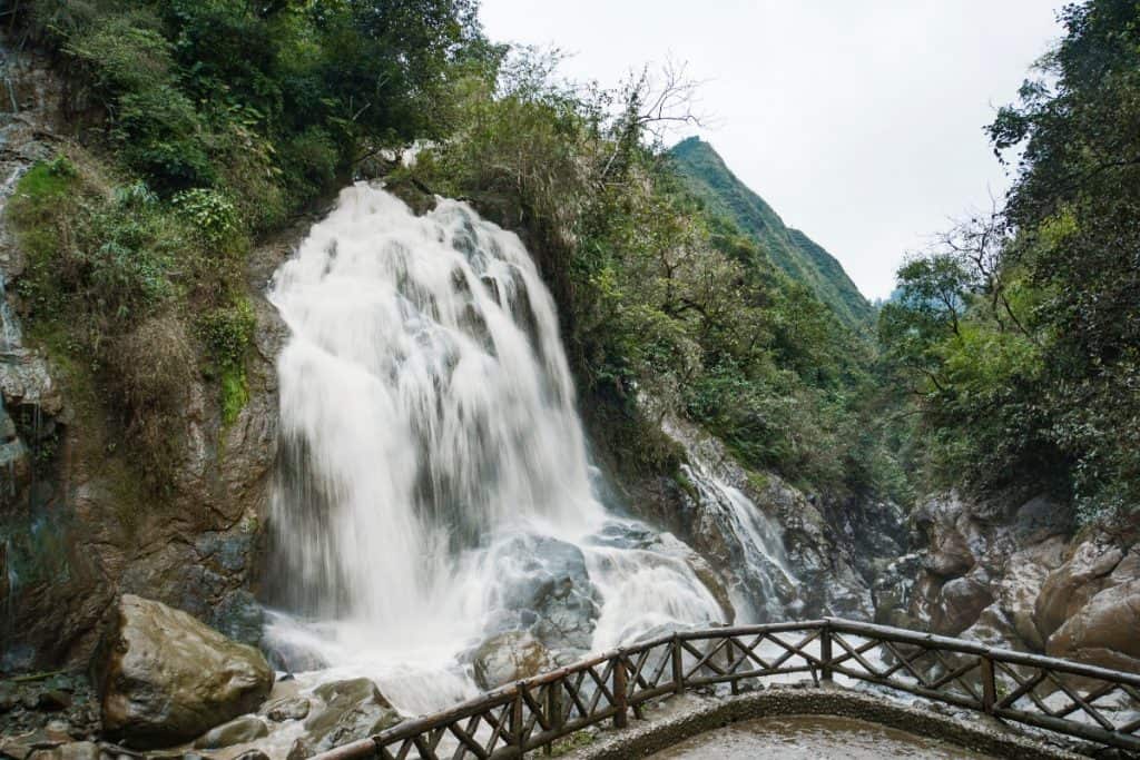 Sapa waterfall cascading amidst lush greenery with mountain views.