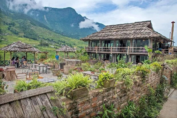 Sapa rustic mountain lodge with lush greenery and scenic backdrop.
