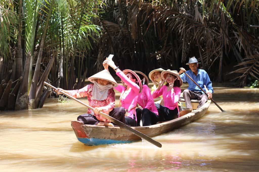 Mekong Delta boat tour with local women in traditional hats exploring lush waterways.