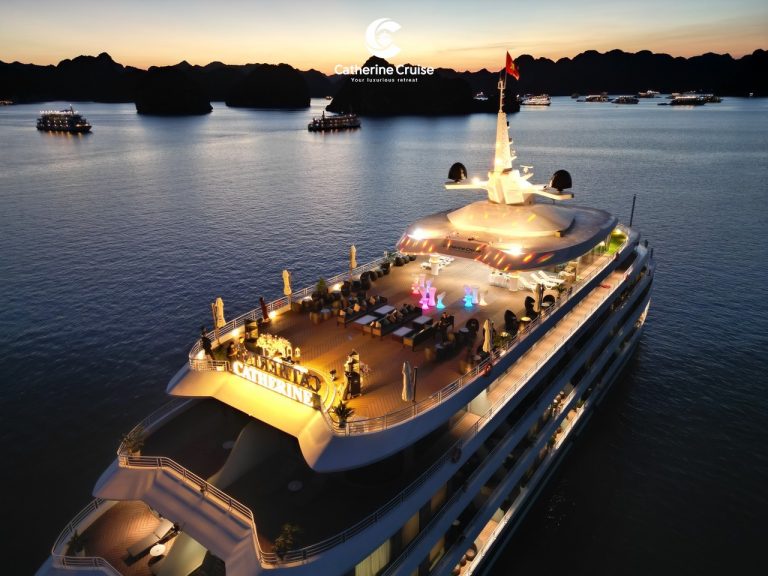 Luxurious cruise ship at sunset in Halong Bay, Vietnam, with scenic island views and vibrant deck lighting.