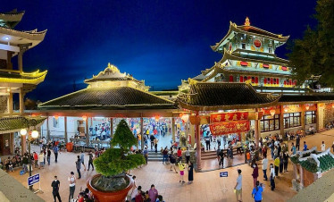 Vietnam temple illuminated at night with vibrant lights and bustling visitors.