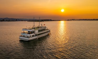 Sunset view of a luxury cruise sailing on Halong Bay at dusk, showcasing tranquil waters and stunnin.