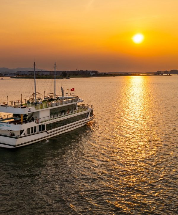 Sunset view of a luxury cruise sailing on Halong Bay at dusk, showcasing tranquil waters and stunnin.