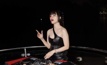 Female DJ performing on a cruise balcony in Halong Bay at night, vibrant and lively atmosphere for t.