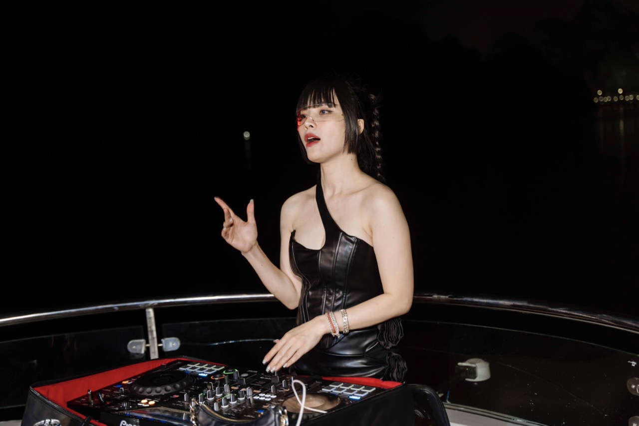 Female DJ performing on a cruise balcony in Halong Bay at night, vibrant and lively atmosphere for t.