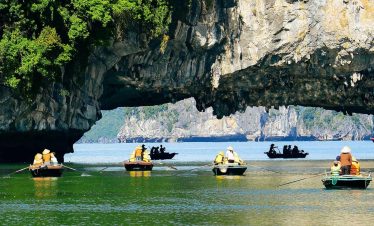 Scenic view of boats kayaking under limestone cliffs in Halong Bay, creating a tranquil travel scene.