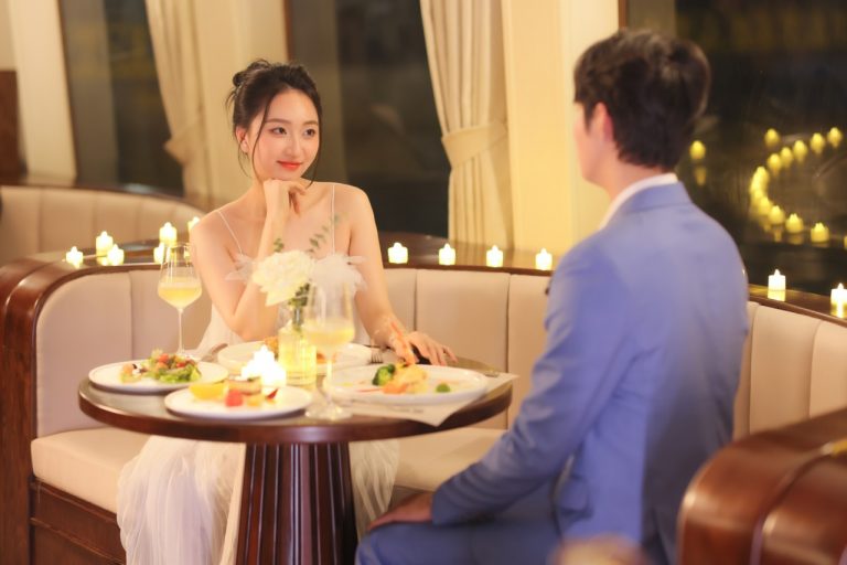 Romantic dinner scene on Halong Bay cruise with couple enjoying a scenic view and fine dining.