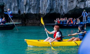 Vivid scene of tourists kayaking in Halong Bay's turquoise waters, surrounded by towering limestone.