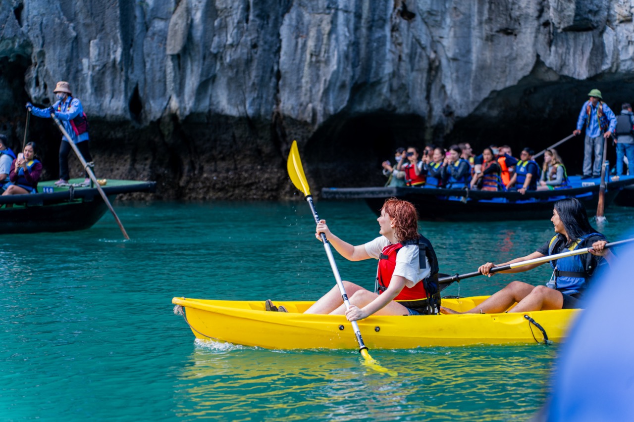 Vivid scene of tourists kayaking in Halong Bay's turquoise waters, surrounded by towering limestone.