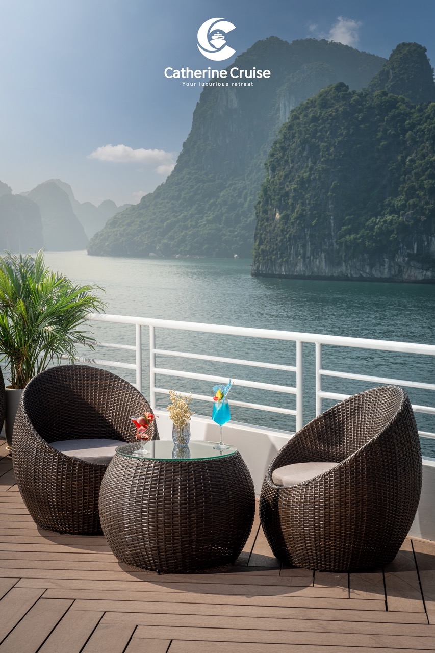 Luxury cruise deck with scenic bay view, wicker chairs, tropical drinks, and mountain landscape.