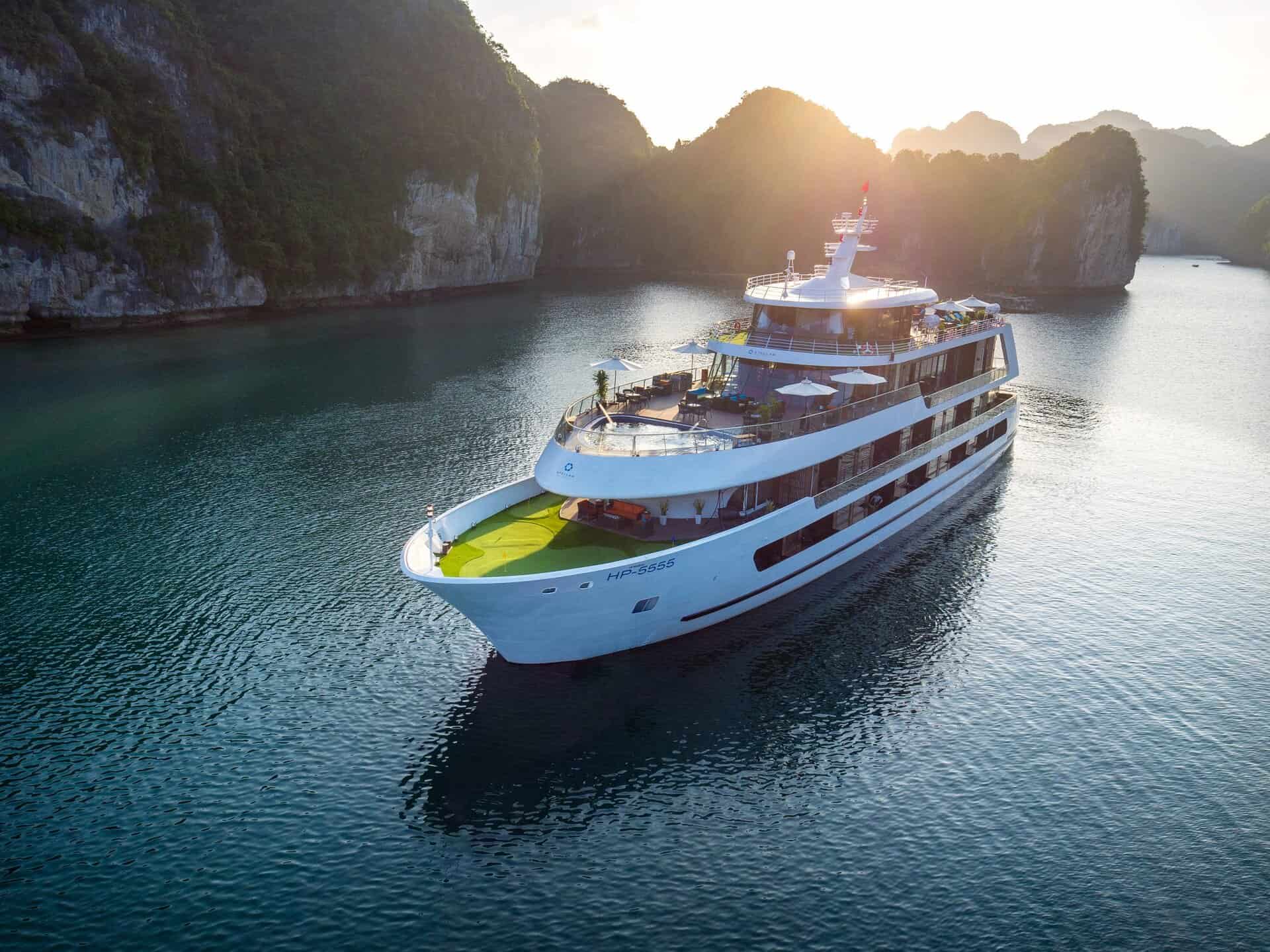 Luxury cruise ship sailing through emerald waters of Halong Bay at sunset.