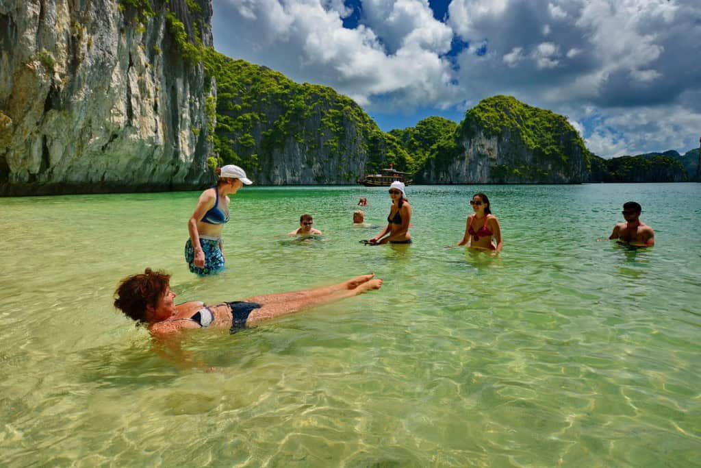 Halong Bay beach scene with tourists enjoying the clear waters and stunning limestone cliffs.