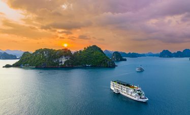 Halong Bay cruise boat sailing during sunset with scenic limestone islands in the background.