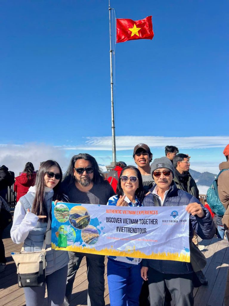 Vietnam tour group holding a banner at a scenic outdoor location with the national flag flying high.