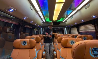 Luxury bus interior with comfortable leather seats and colorful LED ceiling lighting.
