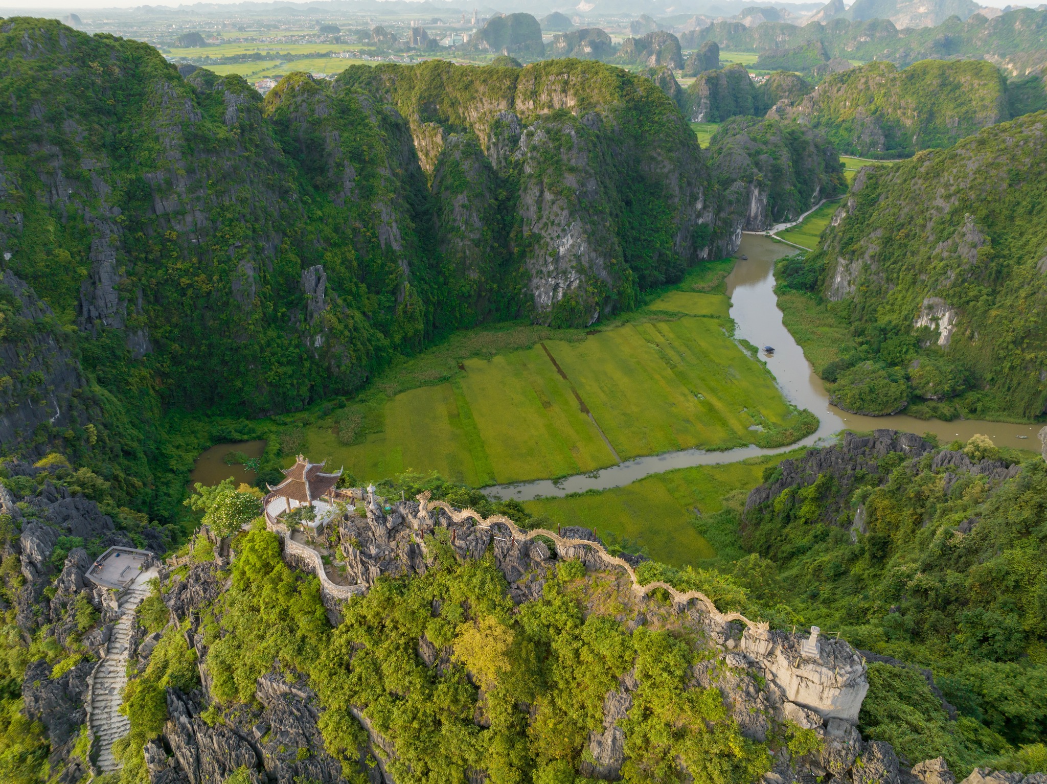 Hanoi countryside landscape with lush green fields, river, and mountains.