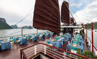 Luxurious cruise deck overlooking Halong Bay with elegant dining setup and traditional sails.