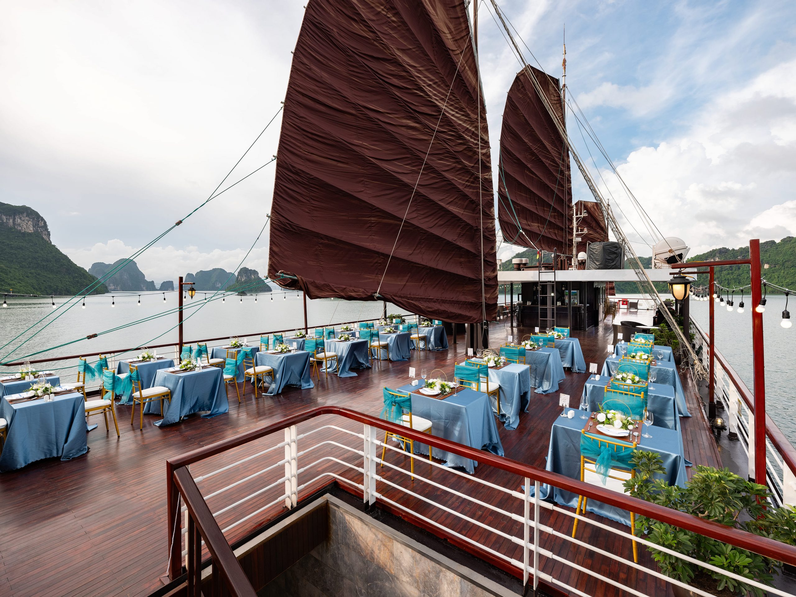 Luxurious cruise deck overlooking Halong Bay with elegant dining setup and traditional sails.