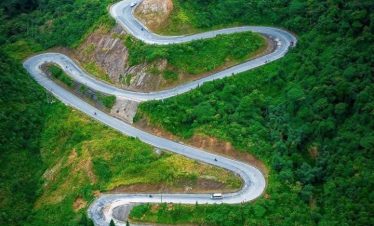Scenic mountain road in Ha Giang with lush greenery and sharp curves, perfect for adventurous travel.