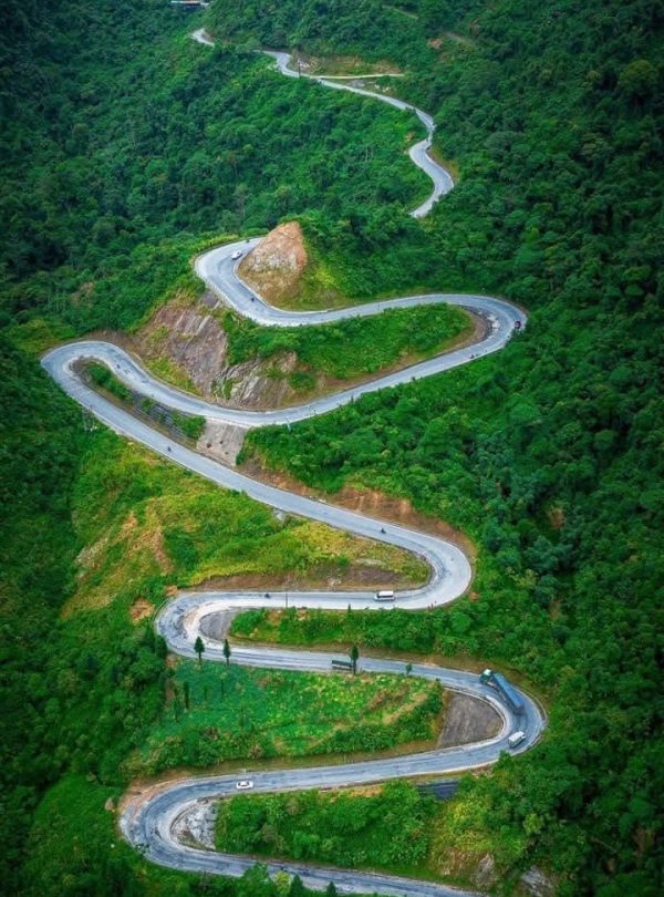 Scenic mountain road in Ha Giang with lush greenery and sharp curves, perfect for adventurous travel.