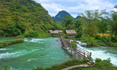 Scenic river scene with lush green mountains and rustic wooden bridge in Ha Giang, perfect for trekk.