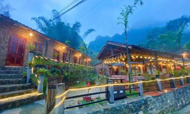 Charming village scene with traditional houses, warm lighting, lush greenery, and misty mountains in.
