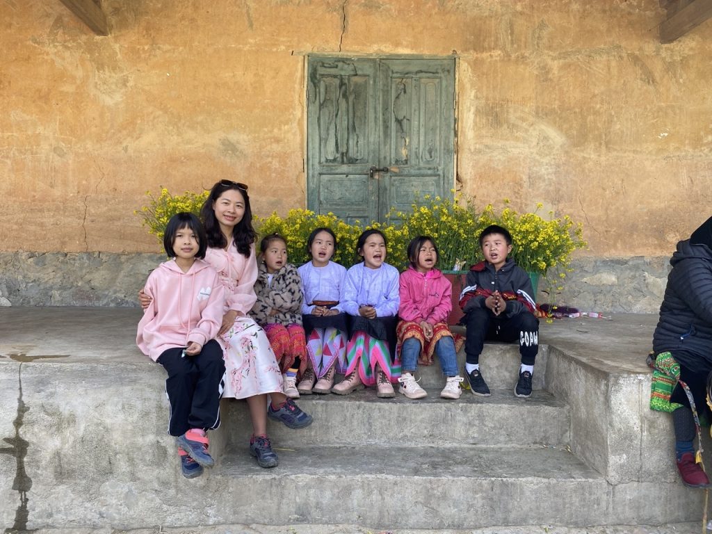 Children and local woman sitting on stone steps in a traditional Vietnamese village, vibrant colors.