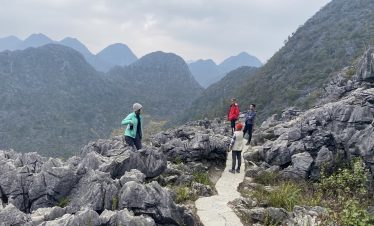 Hiking along rugged mountain trail with travelers enjoying scenic views in Vietnam's lush landscape.