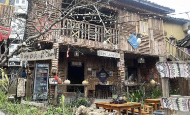 Scenic view of a rustic Vietnamese house with outdoor seating, lush greenery, and cultural charm, pe.
