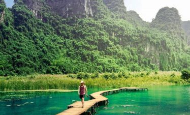 A traveler walking along a wooden pier on Lan Ha Bay with lush green karst mountains in the backgrou.