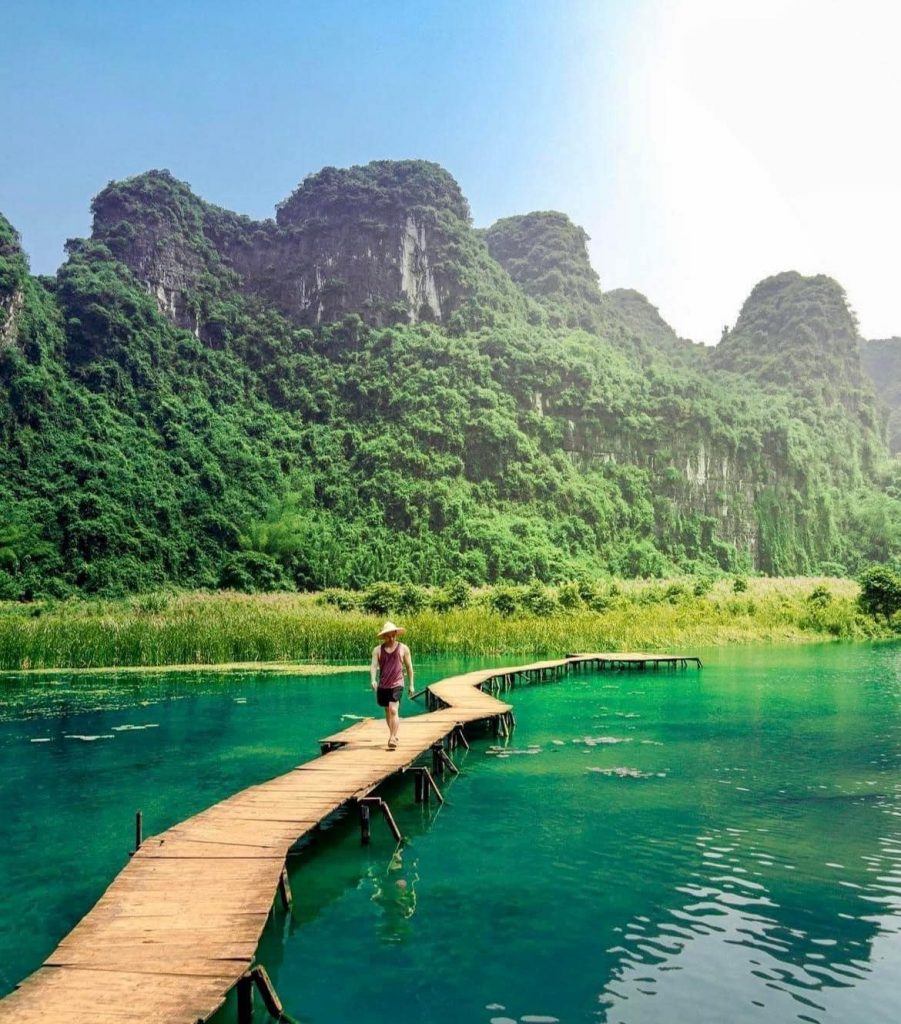 A traveler walking along a wooden pier on Lan Ha Bay with lush green karst mountains in the backgrou.