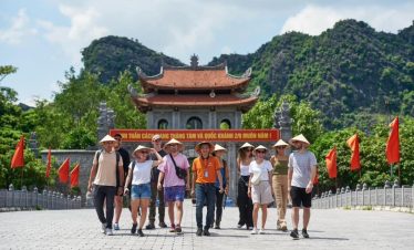 Group of tourists exploring a traditional temple in Vietnam with scenic mountains in the background.