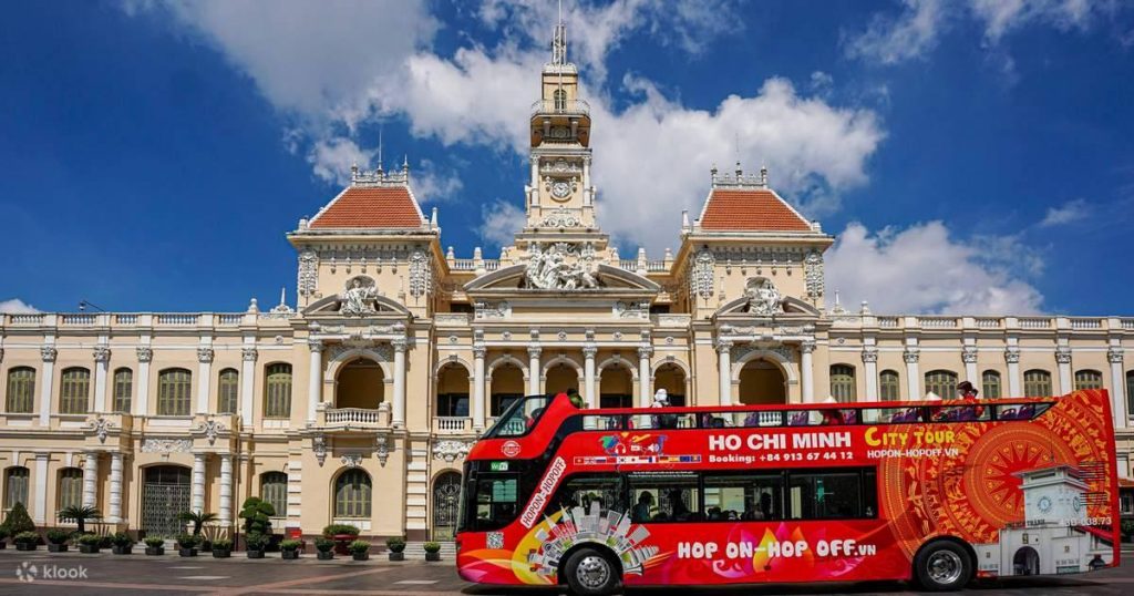 Ho Chi Minh City Tours sightseeing bus with historic architecture in the background.