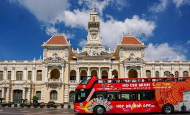 Ho Chi Minh City Tours sightseeing bus with historic architecture in the background.