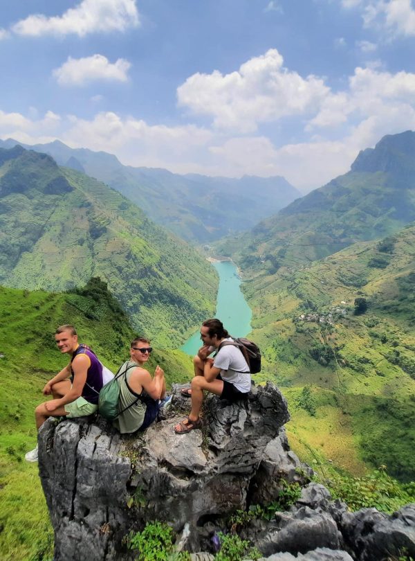 Scenic view of travelers resting on a rocky outcrop overlooking lush green mountains and winding riv.