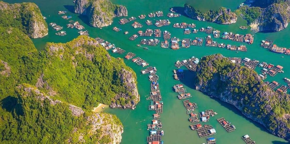 Aerial view of Halong Bay with floating villages, emerald waters, and towering limestone karsts, per.