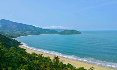 Stunning coastal scenery along Hue to Hoi An route, showcasing lush greenery and tranquil beach view.
