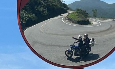 Mirror reflection of winding mountain road with motorbikers in Vietnam, showcasing scenic landscapes.